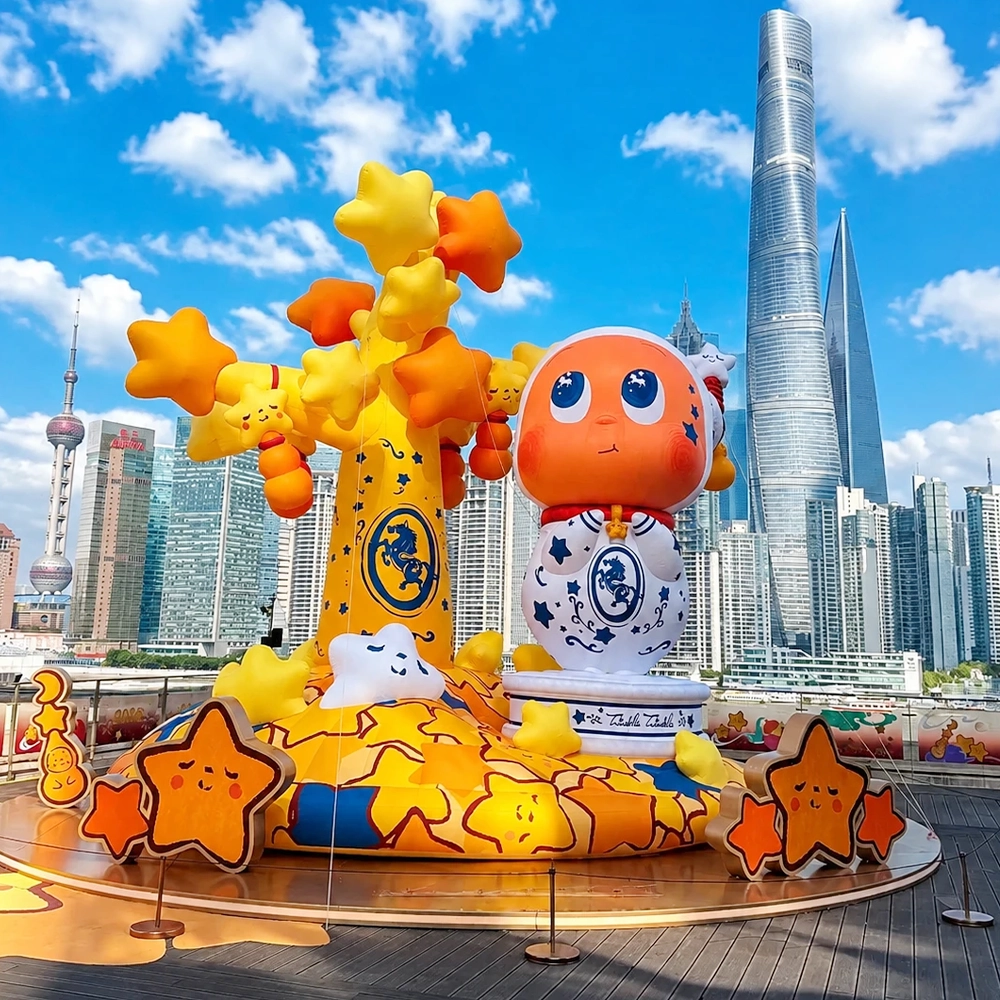 Against the backdrop of a blue sky, the outdoor large-scale fixed inflatable display at Shanghai BFC (Bund Finance Center) features an orange star-shaped IP character, a yellow star-shaped wishing tree, and a cloud-shaped base. The background shows the Shanghai Tower.