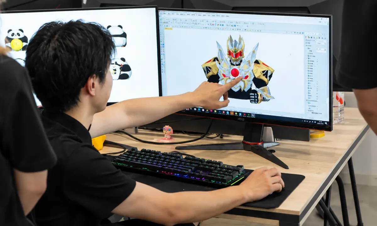 Designer pointing at a 3D inflatable robot character model on a monitor — custom inflatable design review